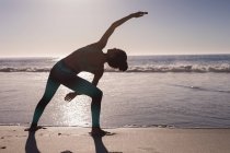 Donna che esegue esercizio di stretching in spiaggia al tramonto . — Foto stock