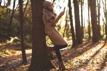 Woman in warm clothing using mobile phone in forest — Stock Photo
