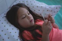 Menina idade elementar usando telefone celular de vidro na cama em casa — Fotografia de Stock