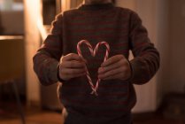 Menino formando forma de coração com bastões de doces em casa — Fotografia de Stock