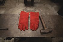 Gants et marteau sur surface métallique en atelier — Photo de stock