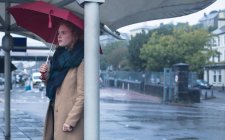 Junge Frau mit Regenschirm steht an einem regnerischen Tag an einer Bushaltestelle — Stockfoto