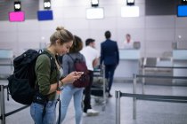 Женщина, стоящая в очереди в аэропорту с помощью мобильного телефона — стоковое фото