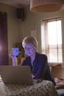 Femme mature utilisant un ordinateur portable tout en prenant un café dans le salon à la maison — Photo de stock