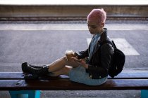 Jovem com cabelo rosa ouvindo música no celular na estação ferroviária . — Fotografia de Stock