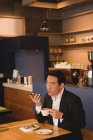 Empresário falando no celular enquanto toma café no café — Fotografia de Stock