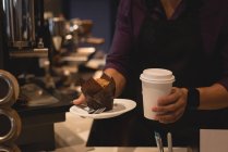 Середня частина офіціанта, що подає каву і кекс у тарілці в кав'ярні — стокове фото