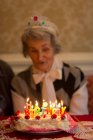 Donna anziana che spegne le candele sulla torta di compleanno a casa — Foto stock