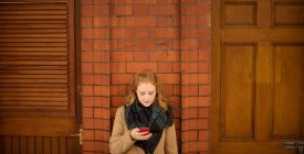Молода жінка використовує мобільний телефон проти стіни — стокове фото
