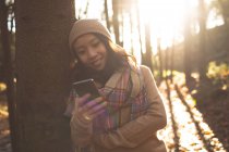 Woman in warm clothing using mobile phone in forest — Stock Photo