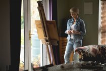 Artista femenina observando pintura sobre lienzo en casa - foto de stock