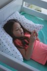 Menina idade elementar usando telefone celular de vidro na cama em casa — Fotografia de Stock