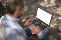 Людина використовує ноутбук у парку в сонячний день — стокове фото