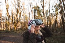 Mulher usando headset realidade virtual na floresta em um dia ensolarado — Fotografia de Stock