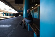 Elegante giovane donna che ascolta musica sul cellulare alla stazione ferroviaria . — Foto stock