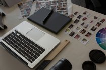 Laptop com tablet gráfico, caneta e fotos na mesa no escritório — Fotografia de Stock