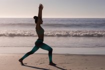 Вмістити жінку, що виконує йогу на пляжі в сутінках . — стокове фото