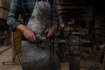 Blacksmith grinding a metal rod with grinder machine in workshop — Stock Photo