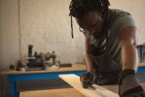 Charpentier mesurant la planche en bois avec ruban à mesurer en atelier — Photo de stock