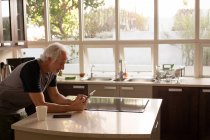 Старший чоловік, використовуючи цифровий планшетний кухні в домашніх умовах — стокове фото