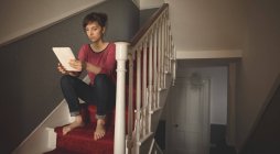 Женщина, использующая цифровой планшет на лестнице дома — стоковое фото