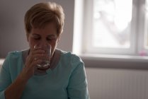 Mujer mayor tomando un vaso de agua en casa - foto de stock