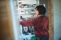 Jovem mulher olhando na geladeira em casa — Fotografia de Stock