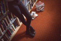 Sección baja de la mujer de pie con las piernas cruzadas en la biblioteca - foto de stock