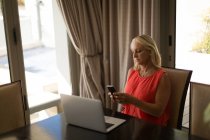 Зріла блондинка використовує мобільний телефон за столом вдома . — стокове фото