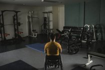 Rear view of handicapped man relaxing on wheelchair in gym — Stock Photo