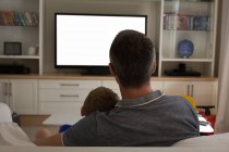 Вид сзади на отца и сына, смотрящих телевизор дома — стоковое фото