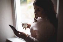 Belle femme utilisant une tablette numérique tout en prenant un café à la maison — Photo de stock