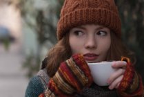 Женщина в зимней одежде, пьет капучино в кафе на открытом воздухе — стоковое фото