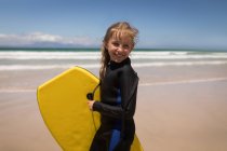 Retrato de menina feliz de pé com prancha de surf na praia — Fotografia de Stock