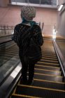 Visão traseira da mulher descendo de uma escada rolante na estação — Fotografia de Stock