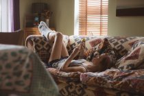 Mulher usando telefone celular enquanto deitado no sofá na sala de estar — Fotografia de Stock