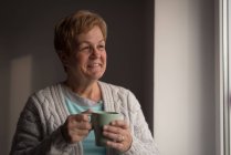 Старша жінка має каву у вітальні вдома — стокове фото