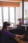 Executivo feminino usando fone de ouvido de realidade virtual enquanto trabalhava no computador na mesa no escritório — Fotografia de Stock