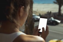 Вид ззаду жінки, використовуючи мобільний телефон вдома перед вікном — стокове фото