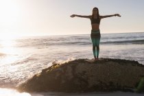 Fit femme effectuant du yoga sur le rocher à la plage au crépuscule
. — Photo de stock