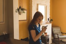 Frau trinkt Kaffee, während sie ihr Handy zu Hause benutzt — Stockfoto