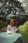 Женщина с цифровым планшетом за столом в саду — стоковое фото