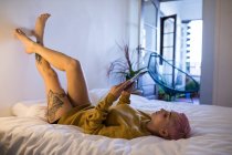 Стильная женщина с цифровым планшетом на кровати в спальне дома . — стоковое фото