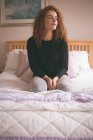 Thoughtful woman sitting on bed in bedroom at home — Stock Photo