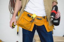 Sección media del carpintero masculino con cinturón de herramientas en el taller - foto de stock