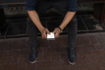 Низкая часть человека с помощью мобильного телефона на тротуарной скамейке — стоковое фото