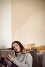 Frau nutzt digitales Tablet auf Sofa im heimischen Wohnzimmer. — Stockfoto