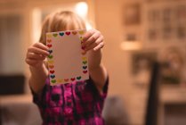 Chica sosteniendo la forma del corazón tarjeta de San Valentín en casa - foto de stock