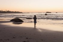 Silhouette di donna che cammina sulla spiaggia sabbiosa al tramonto . — Foto stock
