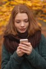 Femme utilisant un téléphone portable dans le parc pendant l'automne — Photo de stock